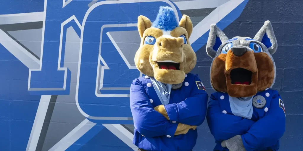 New Kilgore college mascots standing against a wall with a KC logo on it arms folded.